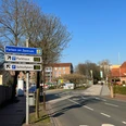 Straßenschild und Bäume entlang einer leeren Straße, die zu einem Parkplatz und Parkhaus führt.