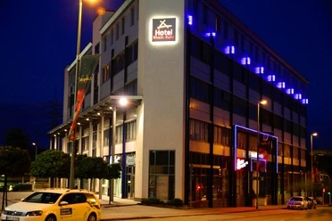Beleuchtetes Hotelgebäude an einer Straße in Bottrop bei Nacht, mit Autos und blauem Neonlicht.