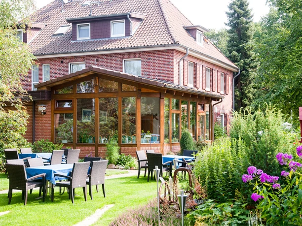 Garten Außenbereich mit Tischen und Stühlen auf einer Wiese vor einem Backsteingebäude mit Wintergarten.