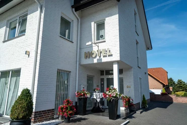 Außenansicht Hotel Papenbreer Weiße, zweistöckige Hotelfassade mit Blumenarrangements im Eingangsbereich bei sonnigem Wetter.