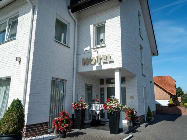 Außenansicht Hotel Papenbreer Weiße, zweistöckige Hotelfassade mit Blumenarrangements im Eingangsbereich bei sonnigem Wetter.