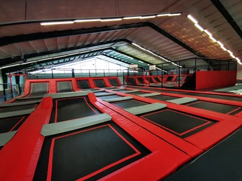 Jump´n Kick innen_Gemeinde Rhauderfehn Große Indoor-Trampolinhalle mit mehreren verbundenen schwarzen und roten Trampolinfeldern unter einem geneigten Dach