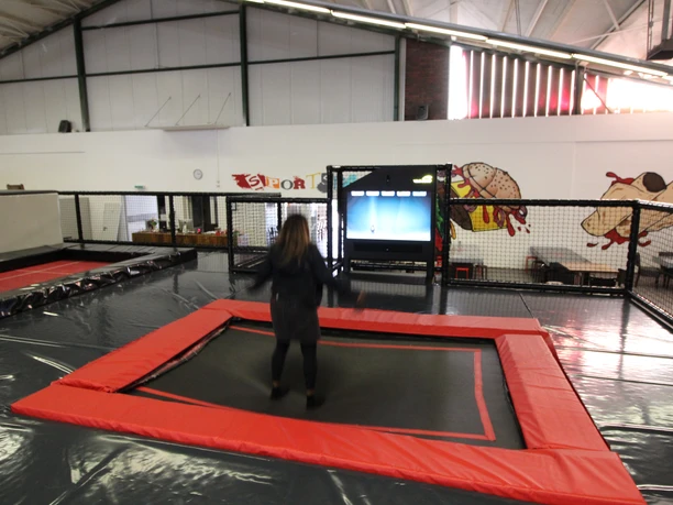 Trampolinhalle Innenbereich Person springt auf einem roten und schwarzen Trampolin in einer Indoor-Sporthalle mit Wandbildern und Spiegeln