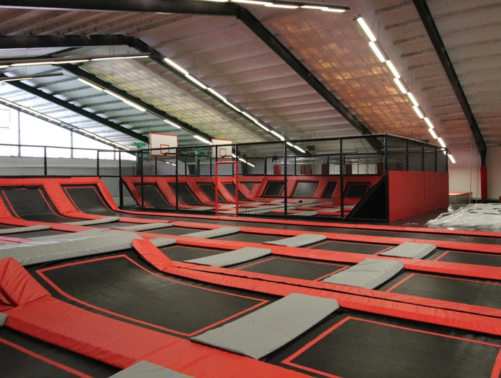 Jump´n Kick innen_Gemeinde Rhauderfehn Große Indoor-Trampolinhalle mit roten und schwarzen Trampolinen und Basketballkörben an der Wand