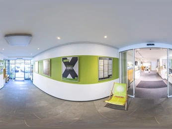 360° Panorama ServiceCenter Gütersloh Flur mit grünen Infowänden, Broschürenregalen und großen Glastüren zum hellen Rundgangsbereich.