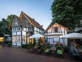 Museumscafé Gütersloh Fachwerkhaus-Restaurant mit Außenbereich, großen Sonnenschirmen, umgeben von Bäumen und Abendhimmel.