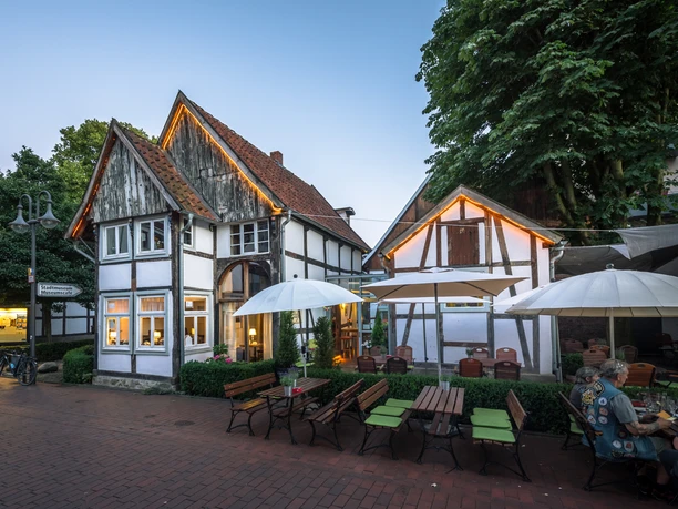 Museumscafé Gütersloh Fachwerkhaus-Restaurant mit Außenbereich, großen Sonnenschirmen, umgeben von Bäumen und Abendhimmel.