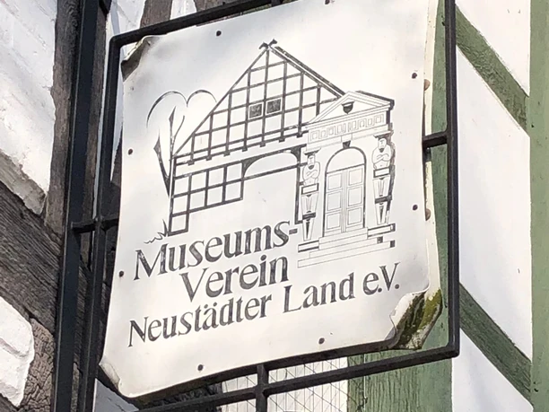Das Bild zeigt ein Schild des Museumsvereins Neustädter Land e.V. an einem Fachwerkgebäude.