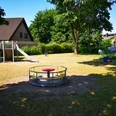 Spielplatz Grillenstraße klein Ein kleiner Spielplatz mit Rutsche, Kletterturm, Wippe und Karussell, umgeben von Bäumen und Wiese.