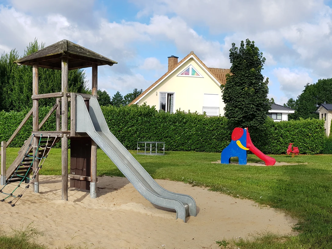 Spielplatz Hermannsweg Spielplatz mit Holz-Klettergerüst, Rutsche, Schaukeln und buntem Spielhäuschen auf Sandfläche.