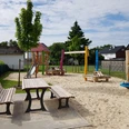 Spielplatz mit buntem Klettergerüst, Rutsche, Schaukeln und Picknicktischen auf hellem Sanduntergrund.
