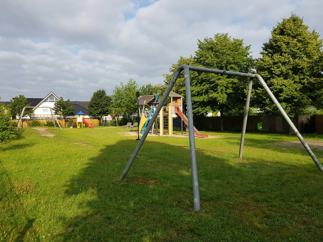 Spielplatz Sophienweg Grüne Wiese mit Klettergerüst und Schaukel in einem ruhigen Wohngebiet unter teils bewölktem Himmel.