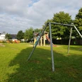 Spielplatz Sophienweg Grüne Wiese mit Klettergerüst und Schaukel in einem ruhigen Wohngebiet unter teils bewölktem Himmel.