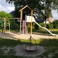 Spielplatz Westfalenweg Ein Spielplatz mit Rutsche und Klettergerät umgeben von Wiesen in einer sonnigen, grünen Umgebung.