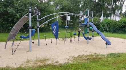 Modernes Klettergerüst auf Sandboden, umgeben von Bäumen, ideal für abenteuerlustige Kinder.