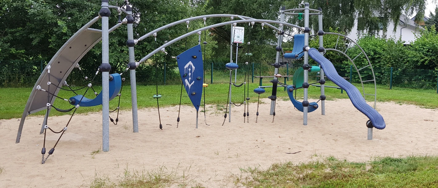 Modernes Klettergerüst auf Sandboden, umgeben von Bäumen, ideal für abenteuerlustige Kinder.