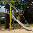 Spielplatz Pirolweg Moderner Spielplatz mit buntem Klettergerüst und Rutsche, umgeben von grünen Bäumen und Rasenflächen.