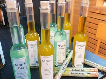 Bärlauch-Varianten Verschiedene Glasflaschen und Röhrchen mit Bärlauchöl, -essig und -salz liegen auf einem dunklen Tisch.