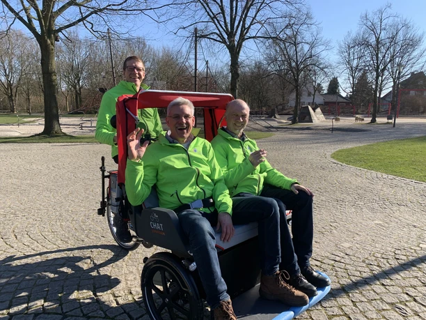 Rikscha-Fahrer Drei fröhliche Männer in leuchtend grünen Jacken sitzen in einer Rikscha auf einem gepflasterten Weg.