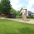 Spielplatz Jostweg Spielplatz mit grüner Wiese, zwei Rutschen, Schaukeln und umgeben von Häusern bei bewölktem Himmel.