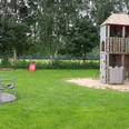Spielplatz Kieselweg Ein grüner Spielplatz mit Kletterturm, Rutsche, Karussell und Schaukeln, umgeben von Bäumen.