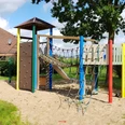 Spielplatz Kranichweg Ein Spielplatz mit Klettergerüst, Rutsche und Kletternetzen auf sandigem Untergrund, umgeben von Natur.