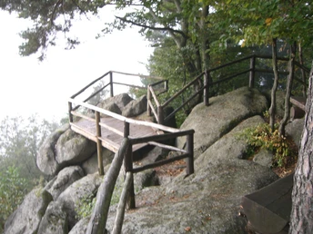Eine Aussichtsplattform aus Holz auf einem Felsen. Im Hintergrund Nebel