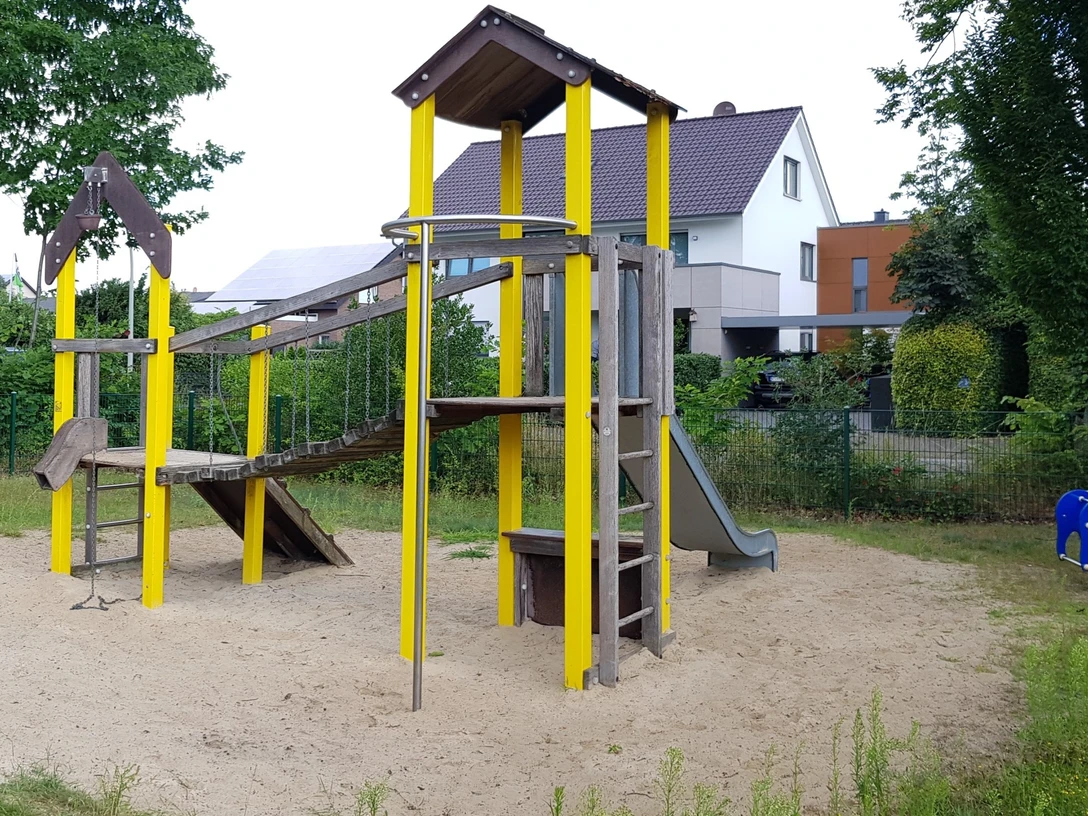 Spielplatz Amselweg Spielplatz in Wohngegend mit Rutsche und Klettergerüst auf Sandfläche, umgeben von Bäumen und Häusern.