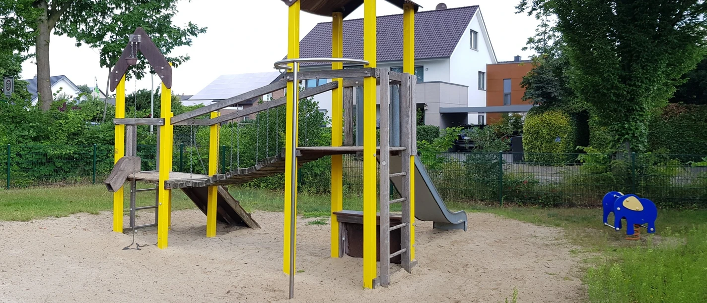 Spielplatz Amselweg Spielplatz in Wohngegend mit Rutsche und Klettergerüst auf Sandfläche, umgeben von Bäumen und Häusern.