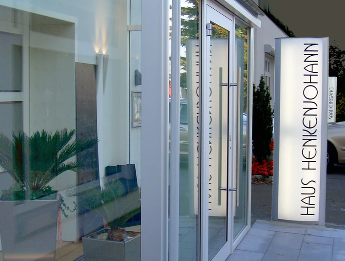 Eingang Haus Henkenjohann Eingangsbereich des modernen Bürogebäudes Haus Henkenjohann mit verglaster Fassade und Pflanzen.