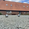 image00009.jpeg Ein rustikales Backsteingebäude mit rotem Ziegeldach im ländlichen Stil; im Vordergrund ein Boulespielfeld mit glänzenden Kugeln und einem kleinen Zielball.