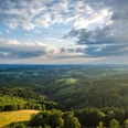 Landschaft am Blockhaus Luftaufnahme einer grünen Hügellandschaft mit ausgedehnten Wäldern und leicht bewölktem Himmel.