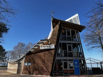 Bistro Meereslauschen Modernes Bistro mit markanter Architektur, Glasfassade und großem Namensschild, umgeben von Bäumen.