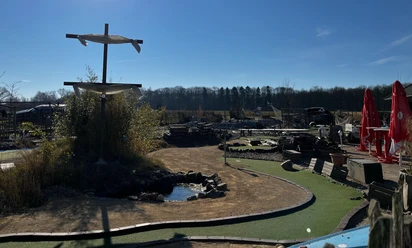 Grünes Minigolfgelände im Activity Park Hagenburg mit Schirmen, Bänken und einem kleinen Teich.
