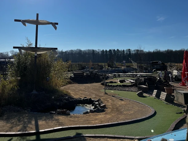 Grünes Minigolfgelände im Activity Park Hagenburg mit Schirmen, Bänken und einem kleinen Teich.