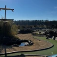 Blick auf das Gelände Activity Park Hagenburg Grünes Minigolfgelände im Activity Park Hagenburg mit Schirmen, Bänken und einem kleinen Teich.