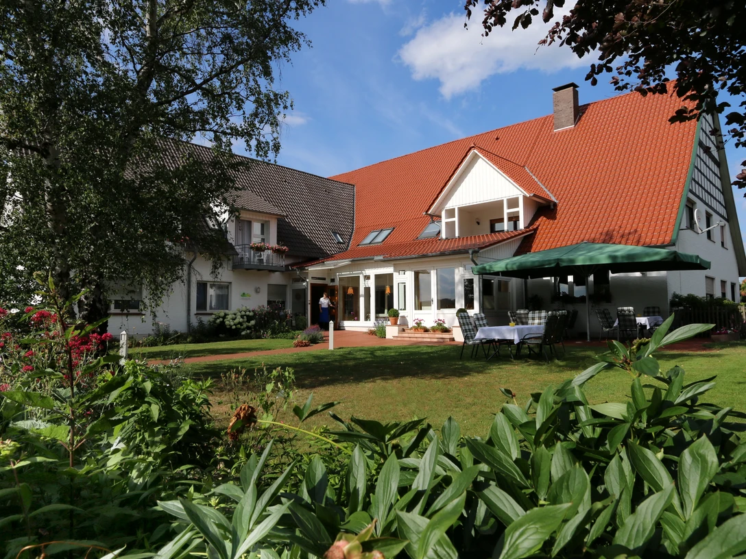 Landhaus Blankenstein Ein Landhaus mit roten Dachschindeln, umgeben von grünen Pflanzen und einem sonnigen, blauen Himmel.