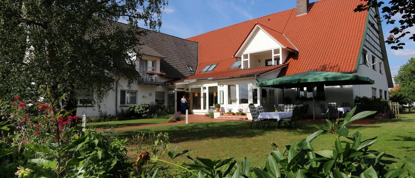 Landhaus Blankenstein Ein Landhaus mit roten Dachschindeln, umgeben von grünen Pflanzen und einem sonnigen, blauen Himmel.