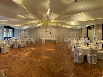 Gasthof Bökamp_Festsaal2 Eleganter Festsaal mit dekorierter Tafel, weißen Stuhlhussen und geschmückter Decke für Feierlichkeiten.