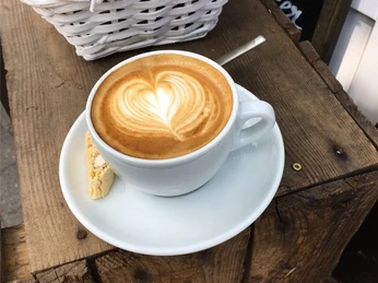 Eine Tasse Cappuccino mit Herzmuster im Schaum, serviert auf einem weißen Unterteller mit Keks.