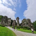 Externsteine_Front_®GesUndTourismus Horn-Bad Meinberg GmbH.jpg Gruppe von Menschen spaziert auf Kiesweg zu massiven Sandsteinfelsen, umgeben von grüner Natur.