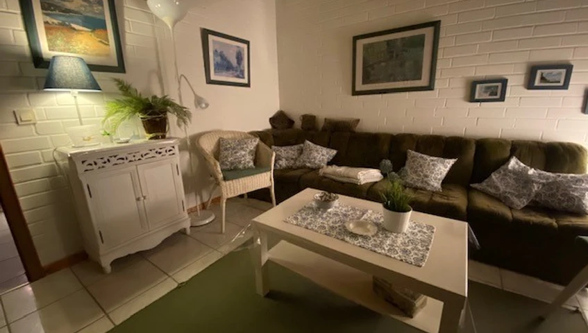 Wohnbereich_01 Gemütliches Wohnzimmer mit grüner Couch, weißen Möbeln und stimmungsvoller Beleuchtung.