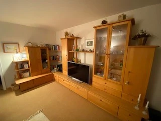Wohnzimmer mit Holzschrankwand, dekorativen Elementen und Fernseher, gemütlich beleuchtet.