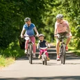 Panoramaradweg Balkantrasse Familie beim entspannten Fahrradausflug auf einem sonnigen, baumgesäumten Weg im Grünen.