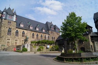 Schloss Burg Historische Burganlage mit Steinmauern, Innenhof und Reiterdenkmal unter blauem Himmel.
