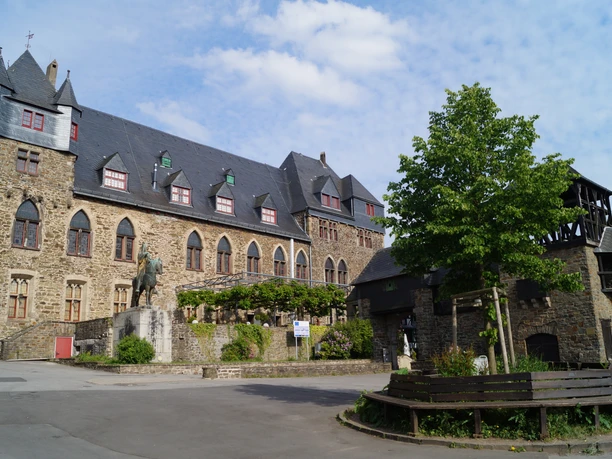 Schloss Burg Historische Burganlage mit Steinmauern, Innenhof und Reiterdenkmal unter blauem Himmel.