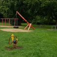 Kinderspielplatz mit grüner Wiese, Schaukeln, Klettergerüst und Bäumen im Hintergrund.