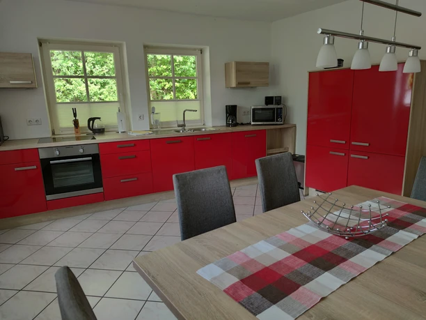 Eine modern ausgestattete Küche mit roten Schränken, Esstisch und großen Fenstern mit Waldblick.