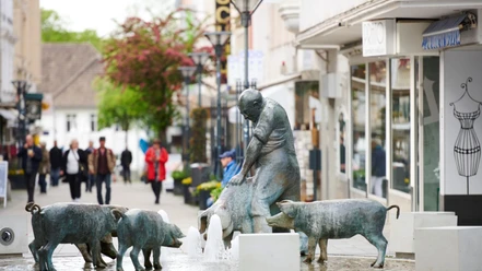 Schweinebrunnen in der Innenstadt Bronzestatue eines Mannes mit Schweinen um einen Brunnen herum in einer belebten Innenstadtstraße.