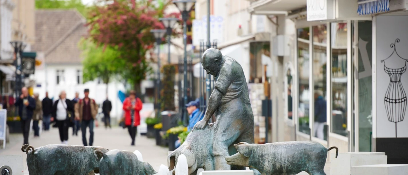 Schweinebrunnen in der Innenstadt Bronzestatue eines Mannes mit Schweinen um einen Brunnen herum in einer belebten Innenstadtstraße.
